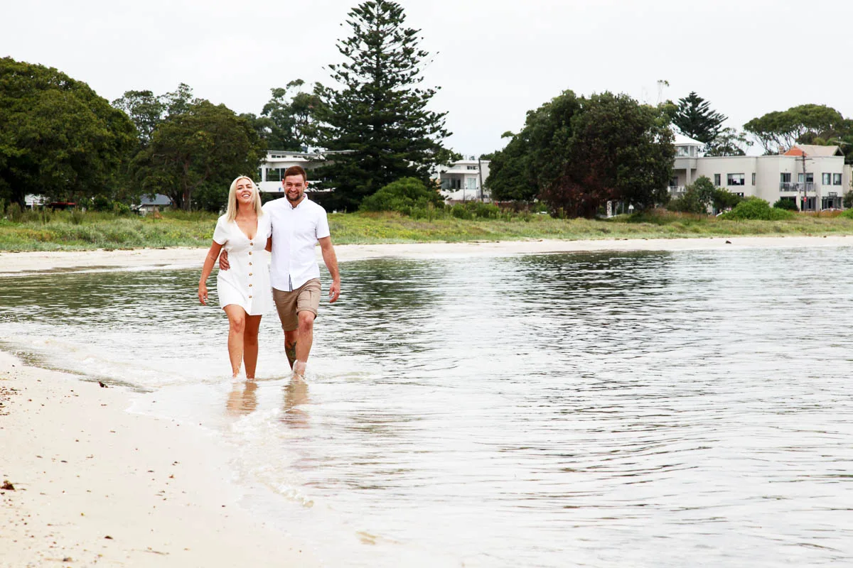 Couple holding hands while walking barefoot through shallow water at the beach during a photoshoot with Southern Exposure Photography in the Sutherland Shire
