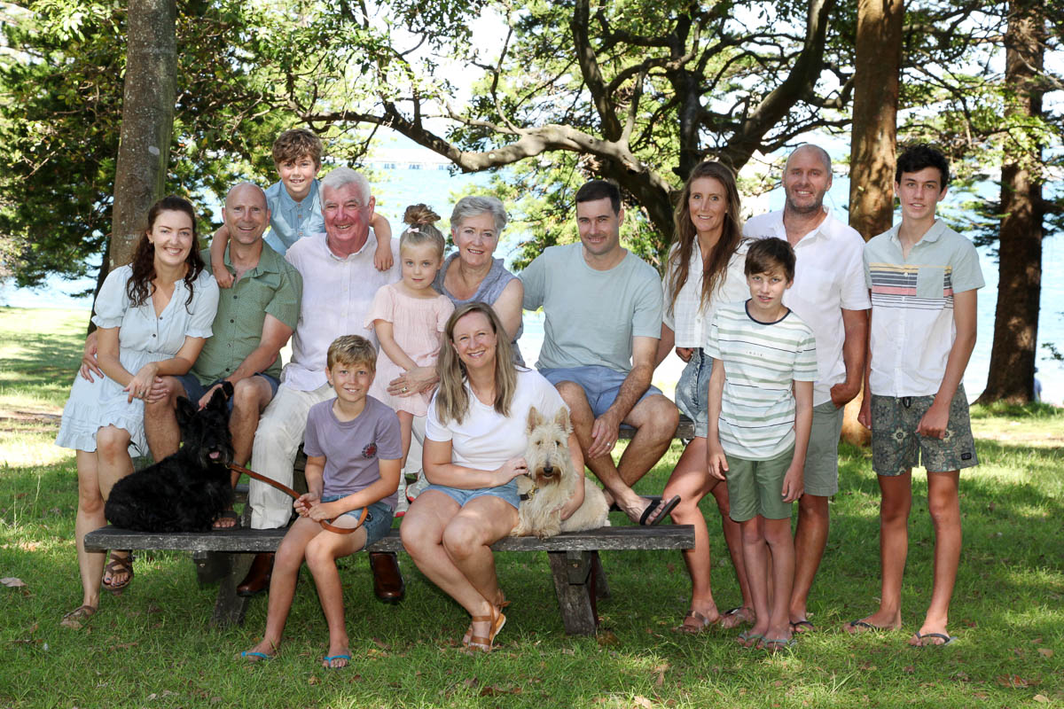 Large extended family group sitting together on a wooden bench in a forested park during an outdoor photoshoot with Southern Exposure Photography in the Sutherland Shire