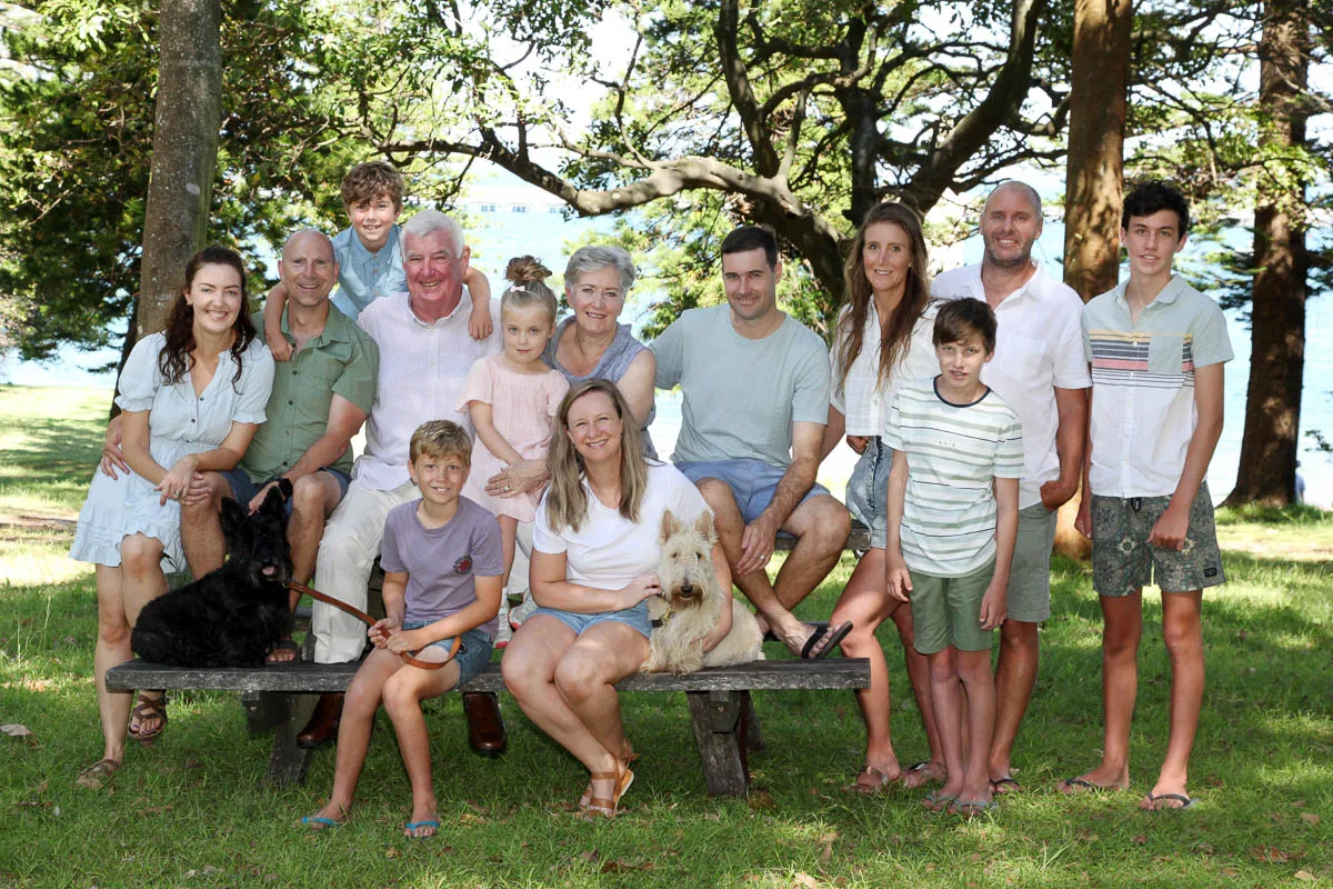 Large extended family group sitting together on a wooden bench in a forested park during an outdoor photoshoot with Southern Exposure Photography in the Sutherland Shire
