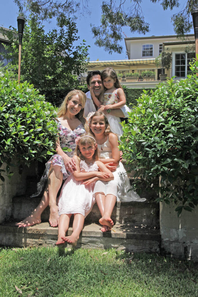 Happy family of five sitting together on garden steps, parents with three young daughters in summer dresses during an outdoor family photoshoot