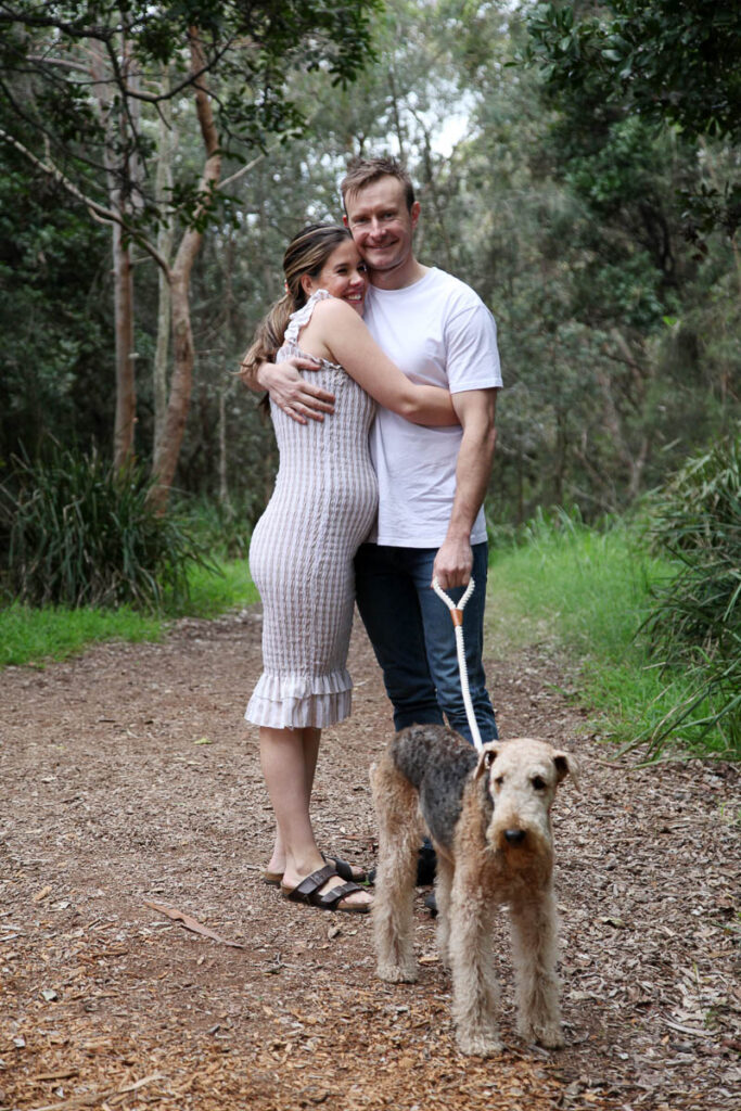 Couple embracing on a forest path with their dog on a lead during a relaxed outdoor family photoshoot with Southern Exposure Photography.
