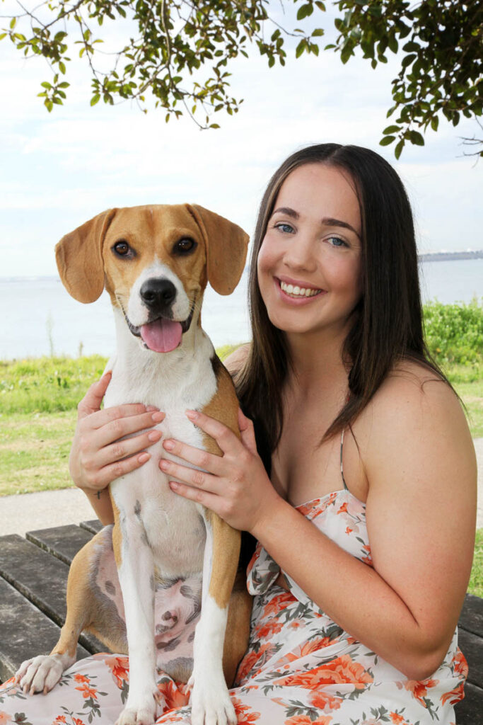 Young woman smiling while holding her dog on a picnic bench by the water during a relaxed outdoor photoshoot with Southern Exposure Photography in the Sutherland Shire