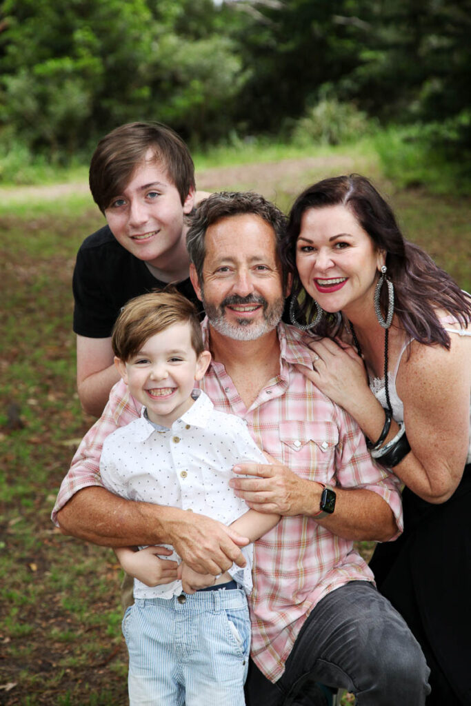 Smiling family of four posing closely together outdoors, with parents and two sons during a relaxed photoshoot by Southern Exposure Photography in the Sutherland Shire