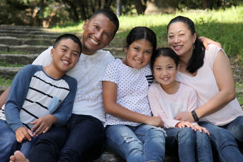 Happy family sitting close together outdoors, smiling warmly during a relaxed photoshoot with Southern Exposure Photography