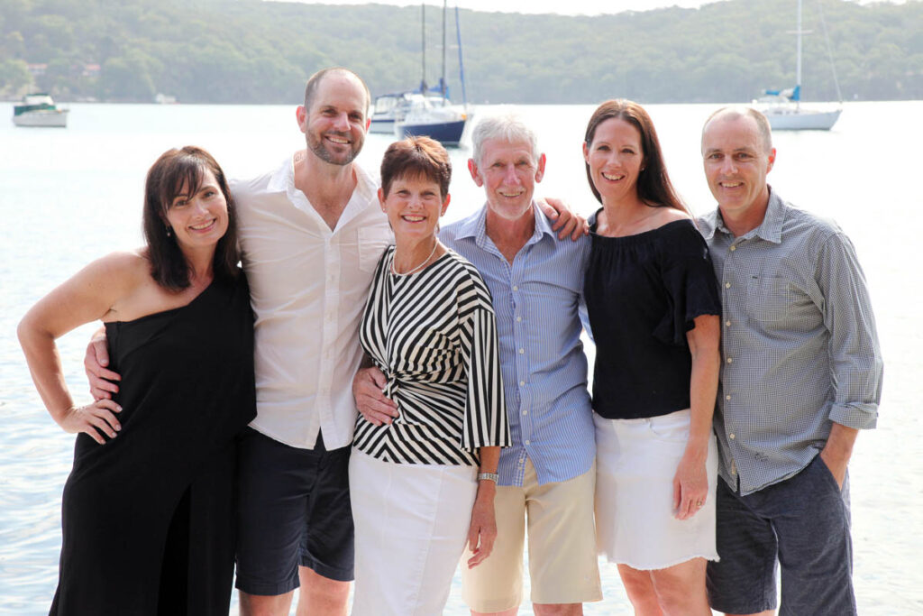 Group of six adults smiling together by the water with yachts in the background during a family photoshoot with Southern Exposure Photography in the Sutherland Shire